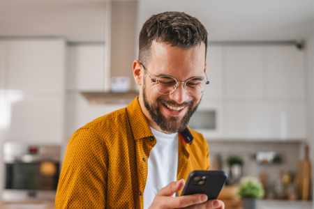 man smiles holding cell phone kitchen