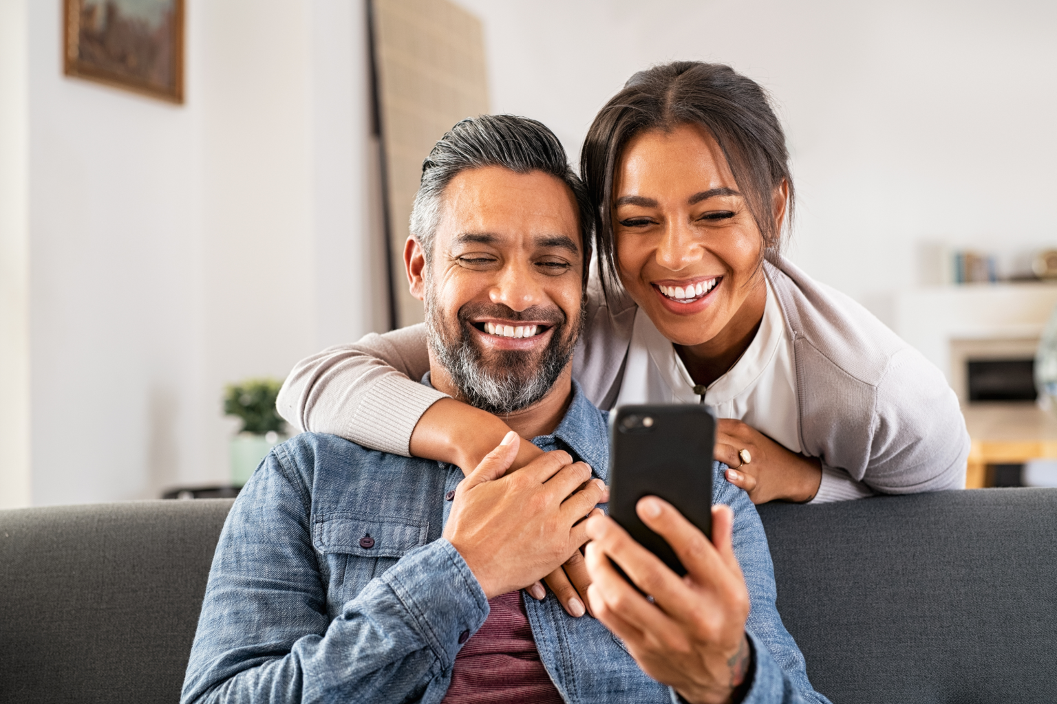 happy couple home smiles viewing mobile phone