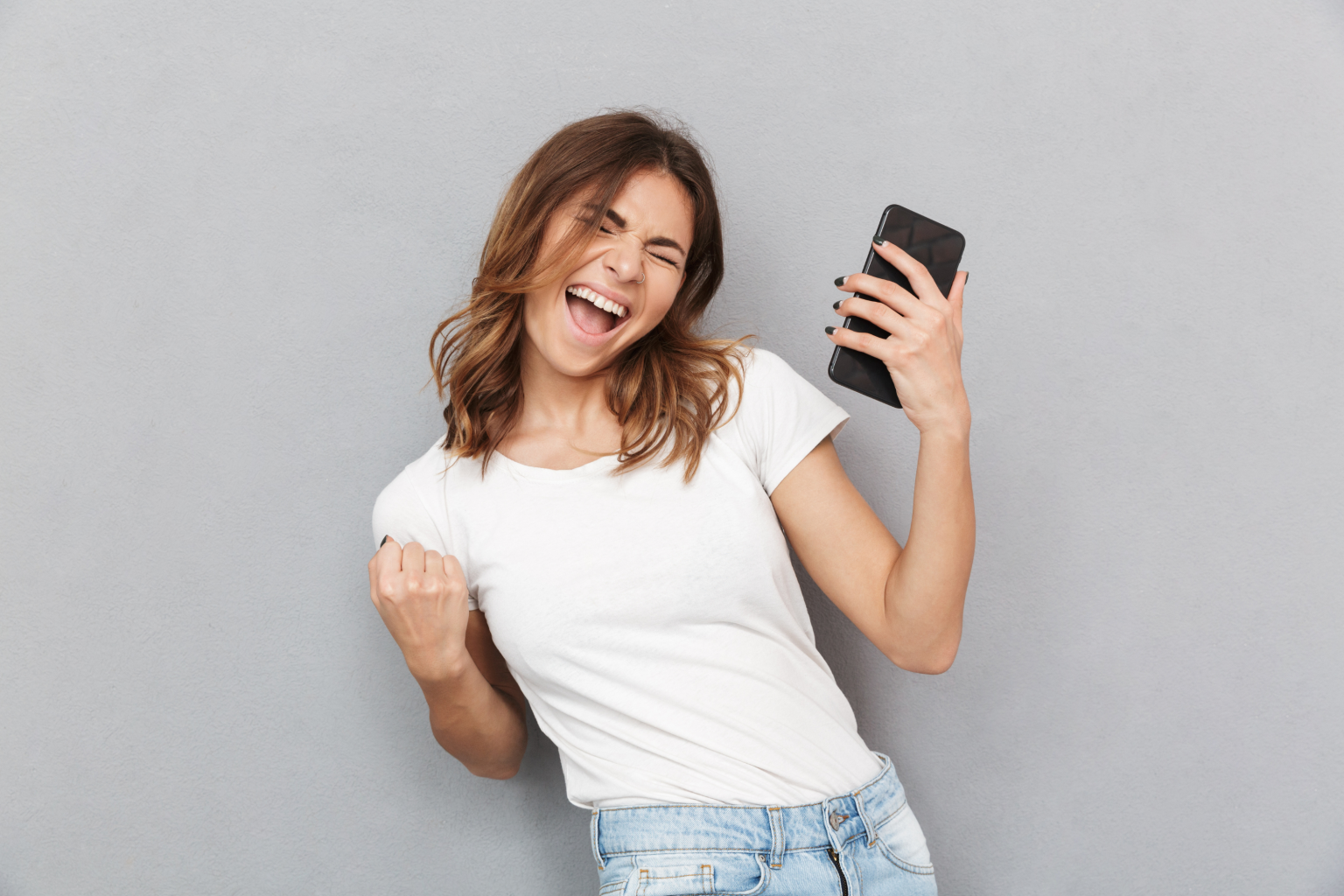 woman celebrating white t shirt blue jeans phone