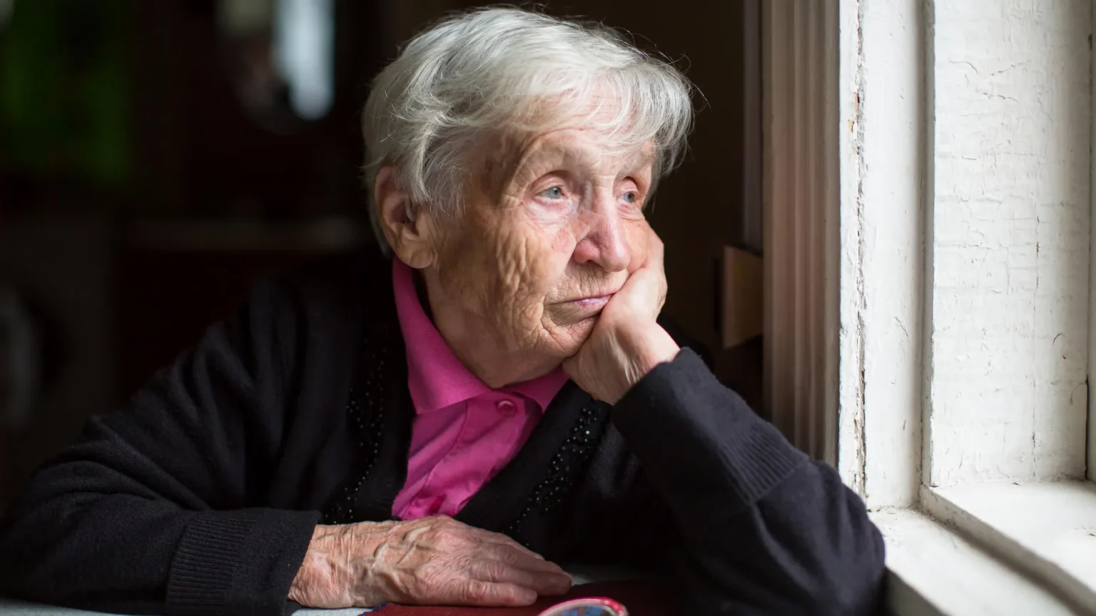 sad elderly woman looking out window.webp